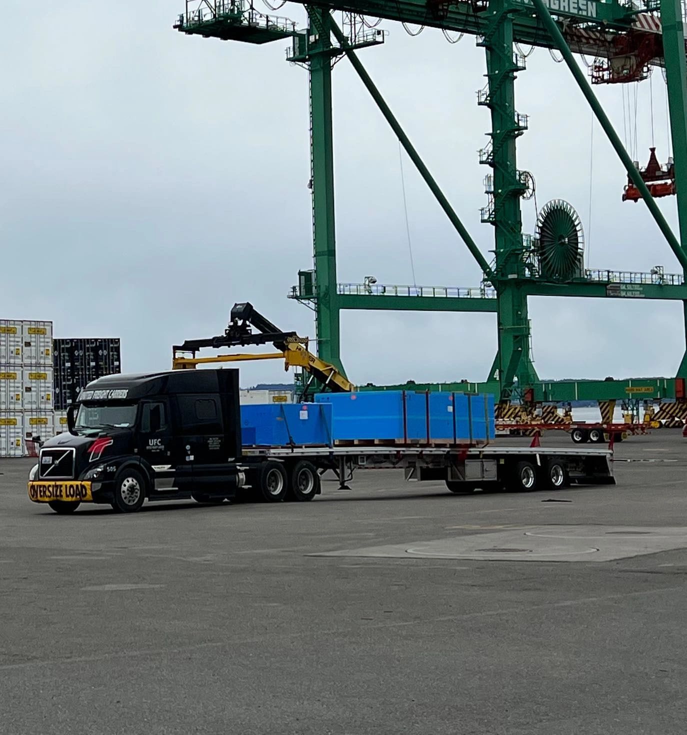 Black truck with oversize load at port with gantry cranes