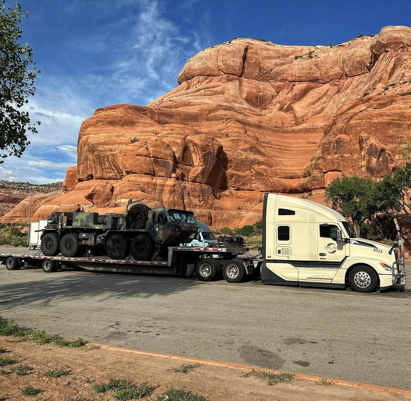 UFC truck hauling military vehicle through desert landscape